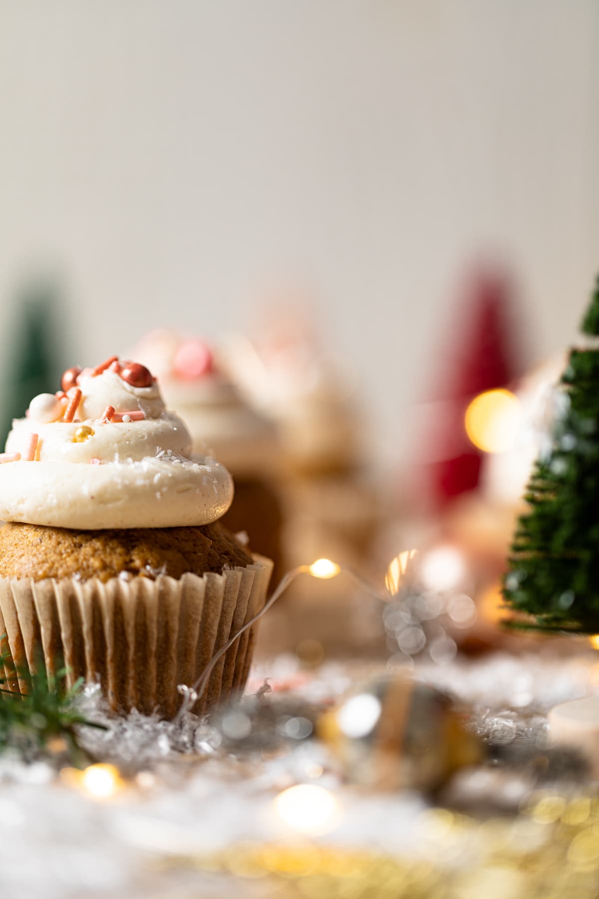 Gingerbread Cupcakes with Eggnog Frosting on a table with Christmas decorations including lights and a small tree