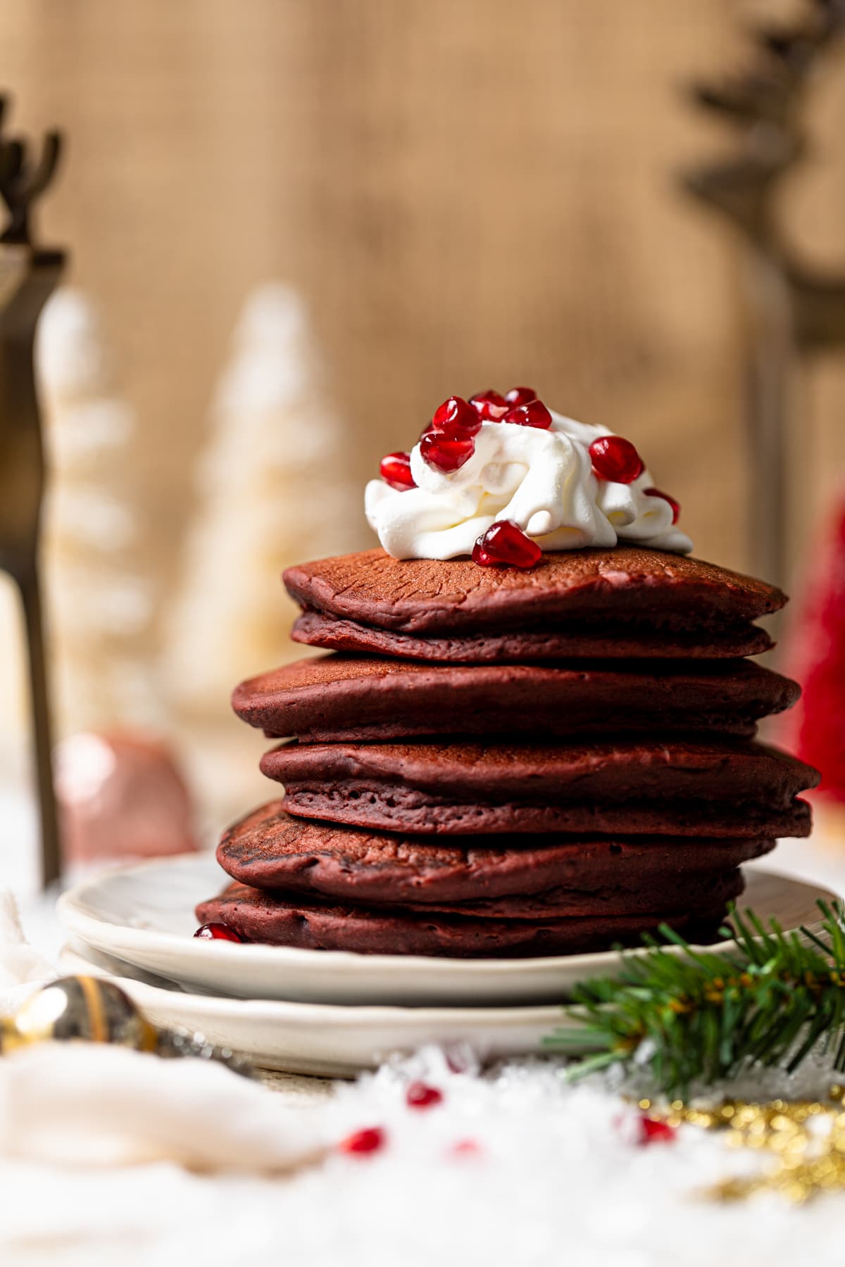 Stack of Fluffy Red Velvet Pancakes topped with whipped cream and pomegranate seeds on two plates