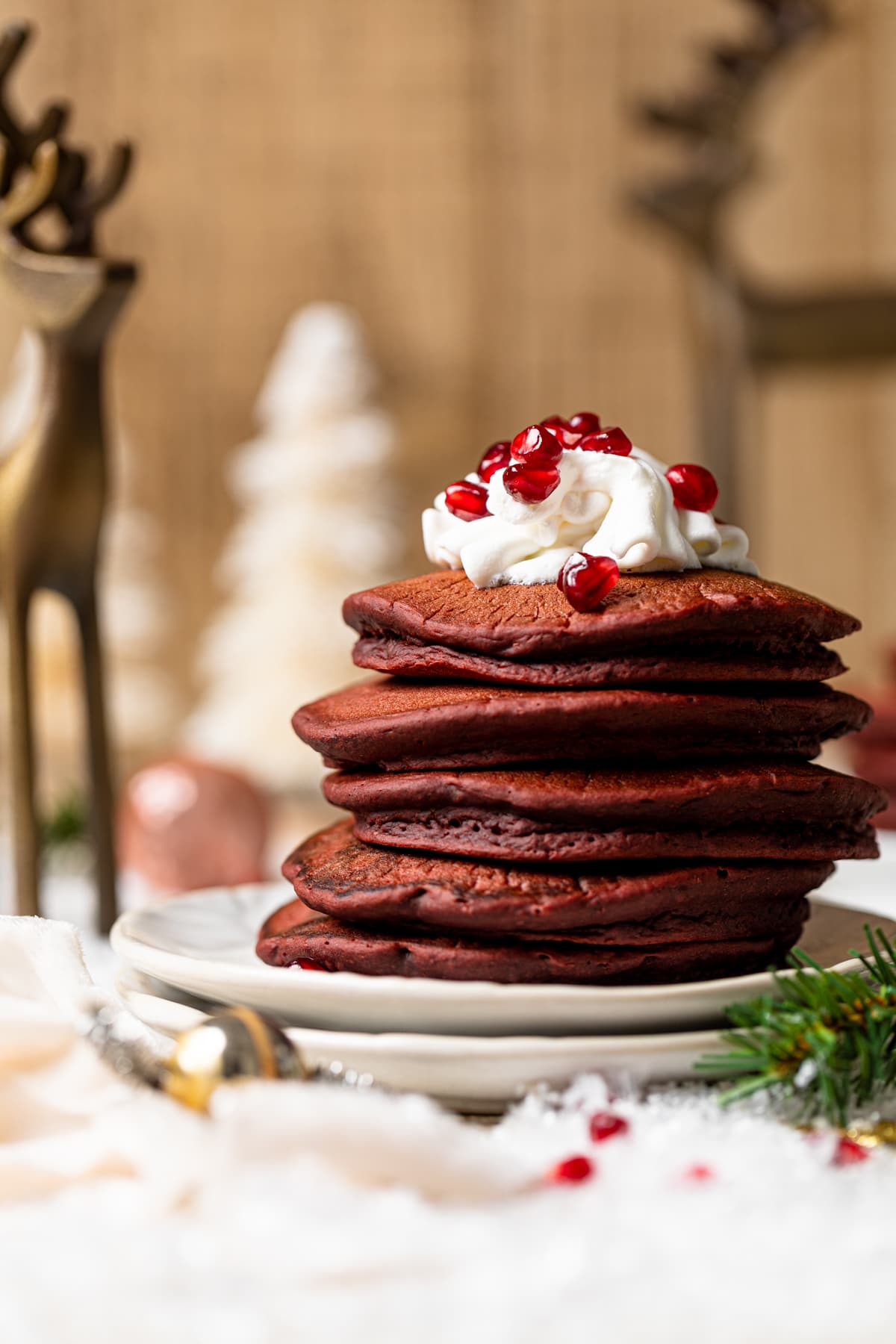 Stack of Fluffy Red Velvet Pancakes topped with whipped cream and pomegranate seeds on two plates