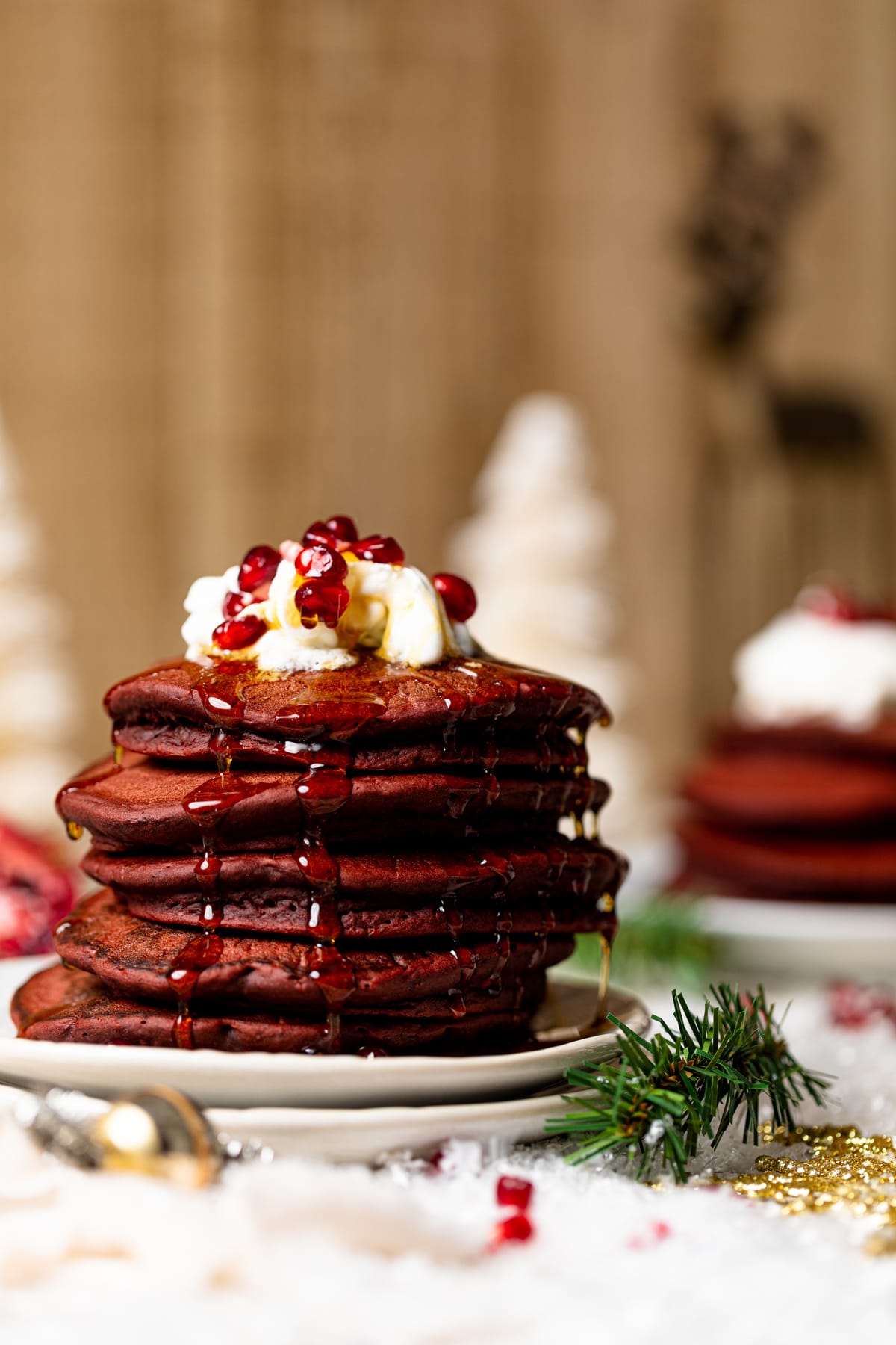 Stack of Fluffy Red Velvet Pancakes topped with whipped cream, syrup, and pomegranate seeds