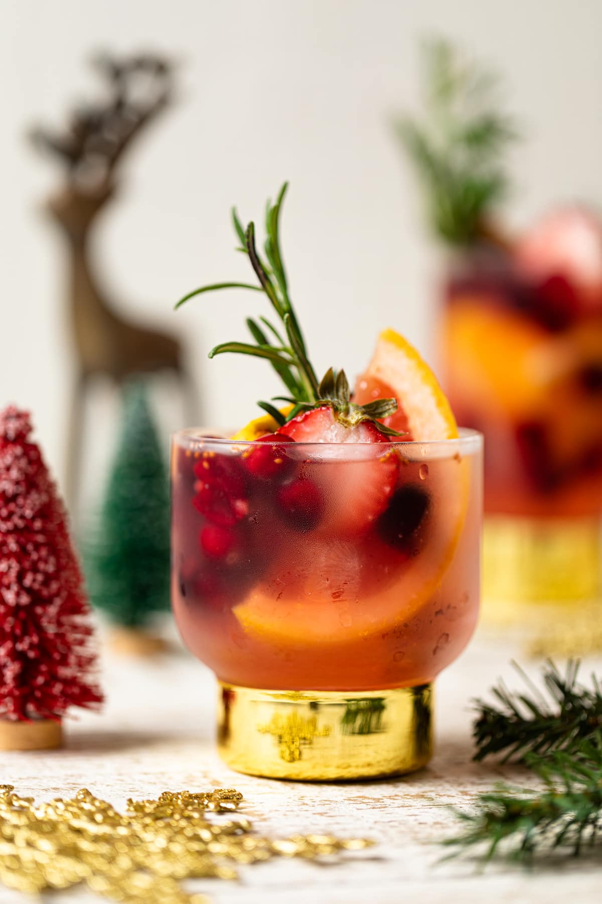 Holiday Mocktail stuffed with cranberries, strawberries, rosemary, and blood orange in a small glass with a golden base