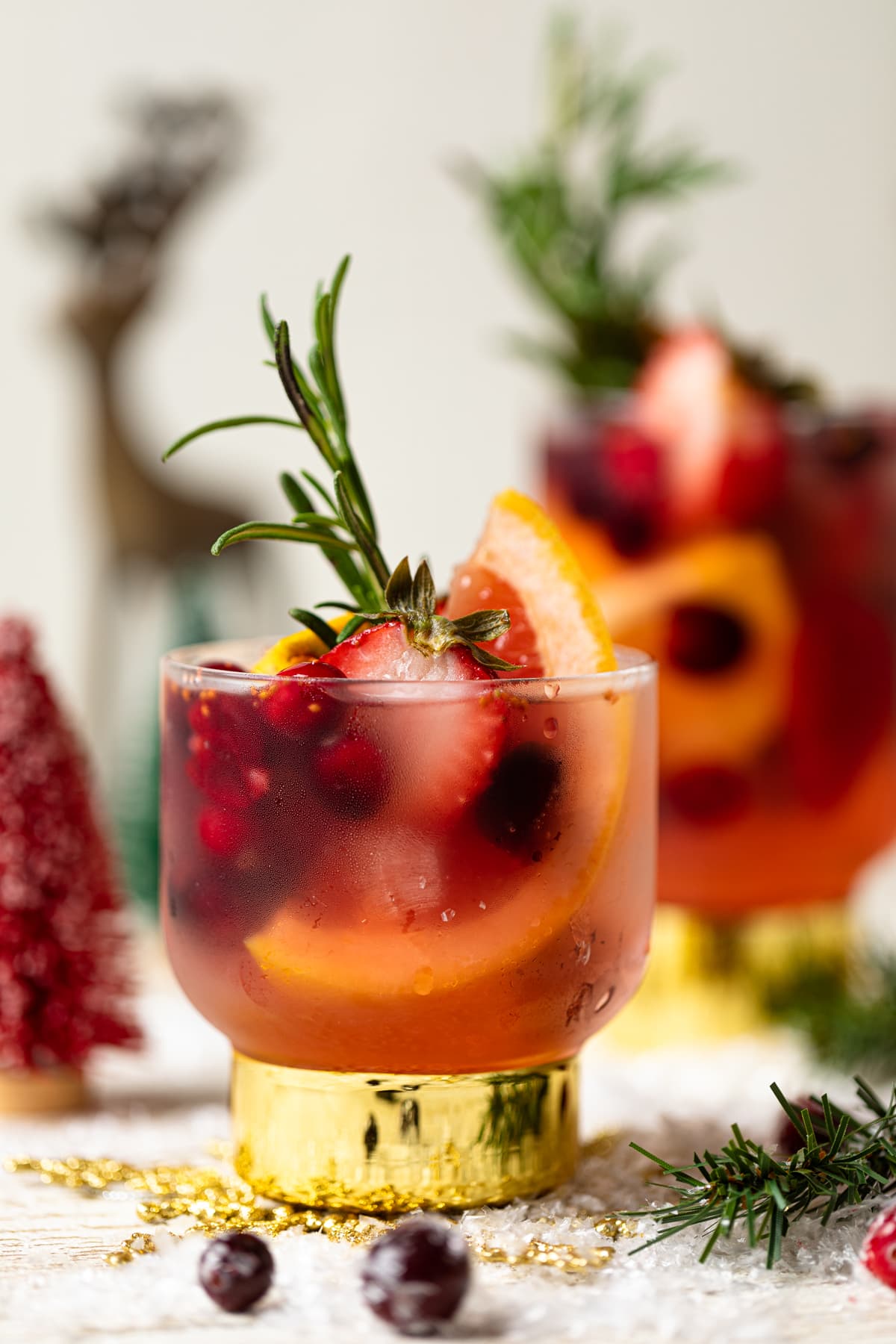 Holiday Mocktail stuffed with cranberries, strawberries, rosemary, and blood orange on a table with Christmas decorations