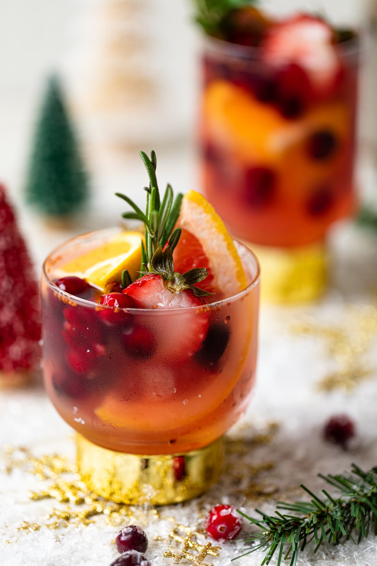 Holiday Mocktail stuffed with cranberries, strawberries, rosemary, and blood orange on a table with Christmas decorations