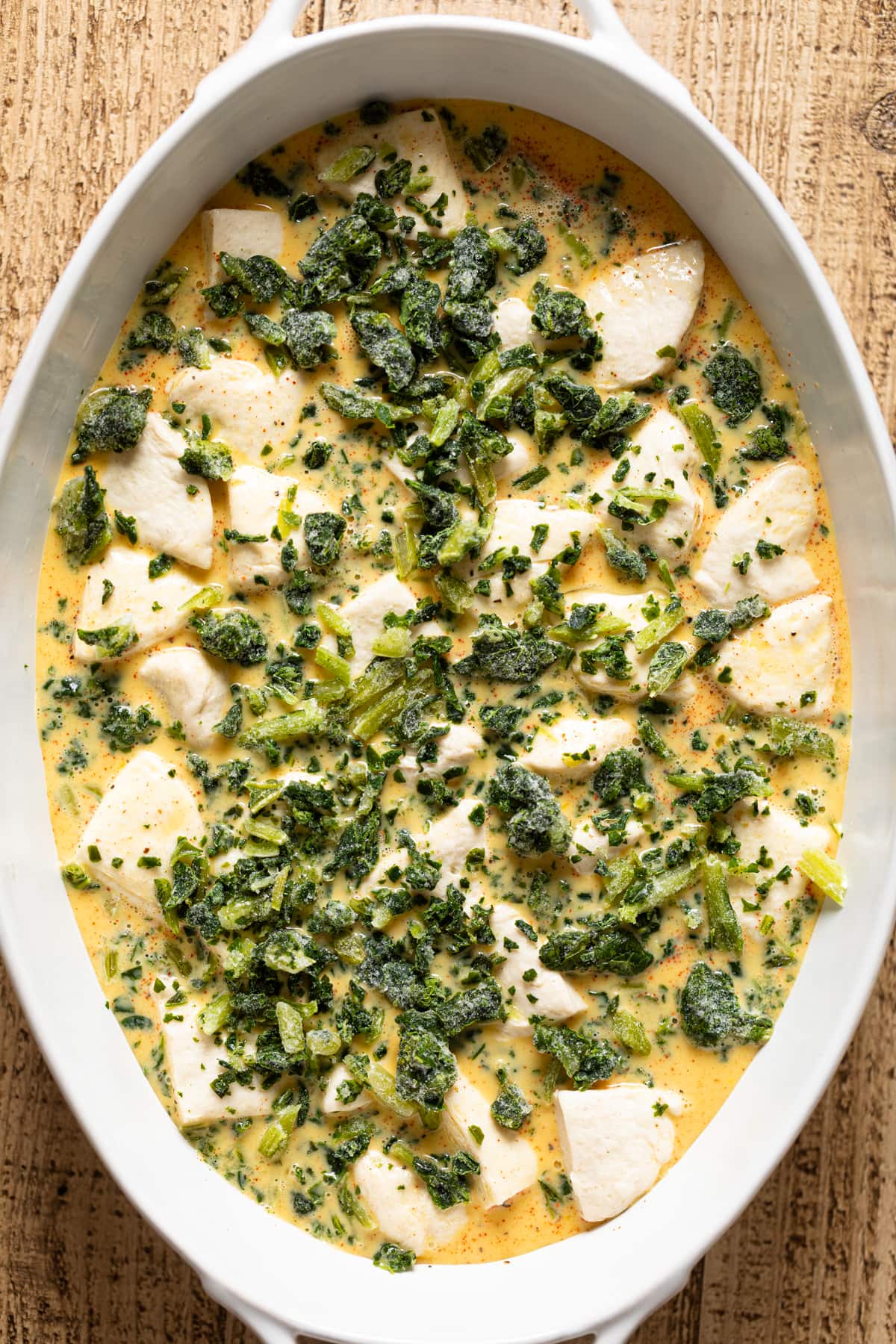 Kale on top of strata batter and biscuit dough in a baking dish