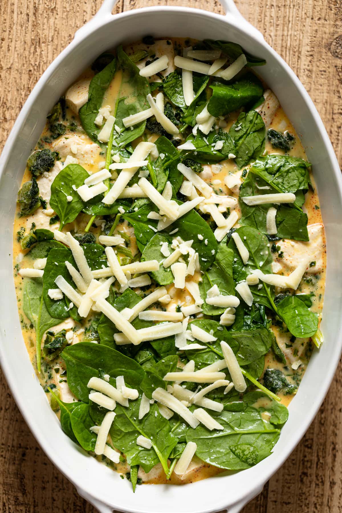 Spinach and shredded cheese on top of the other strata ingredients in a baking dish