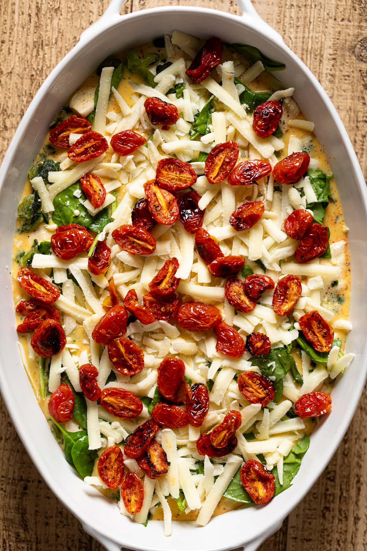 Roasted tomatoes sitting on top of the other strata ingredients in a baking dish