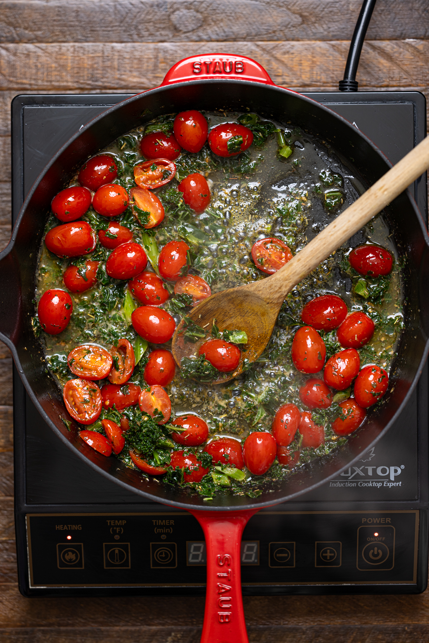 Tomatoes and herbs in a skillet with a wooden spoon being cooked over the stovetop.