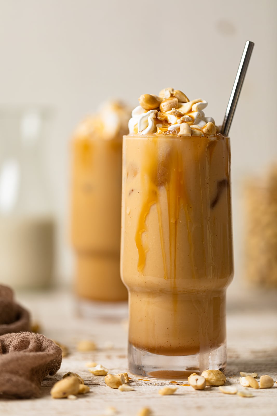 Salted Caramel Cashew Latte with a straw in a tall glass with caramel dripping down the side