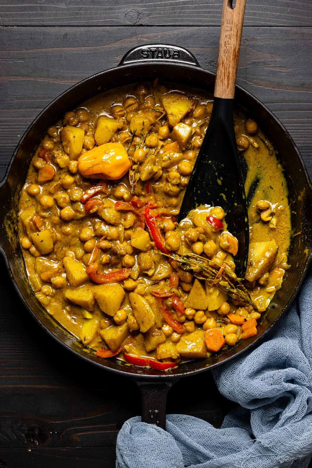 Curry chickpeas and potatoes in a black skillet with a spoon.