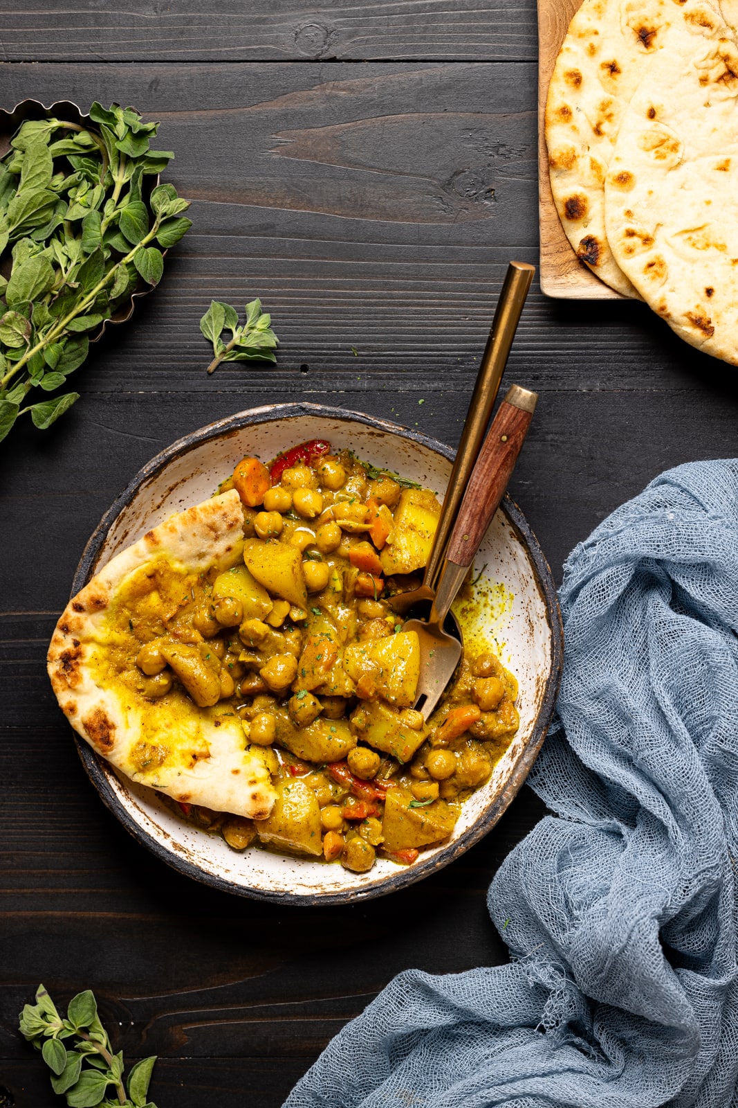 Curry food in a white bowl with two forks and naan bread on the side.