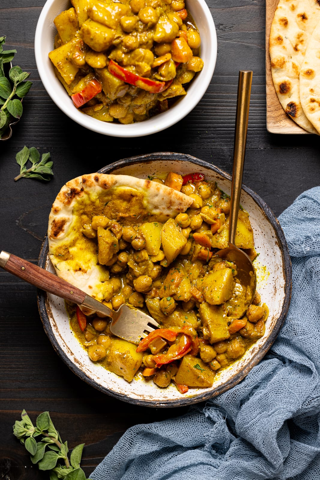 Curry chickpeas and potatoes in a two white bowls with two forks on a black wood table.