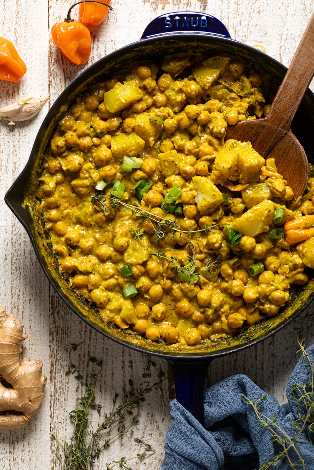 Wooden spoon stirring a skillet of Spicy Curry Chickpea and Potatoes