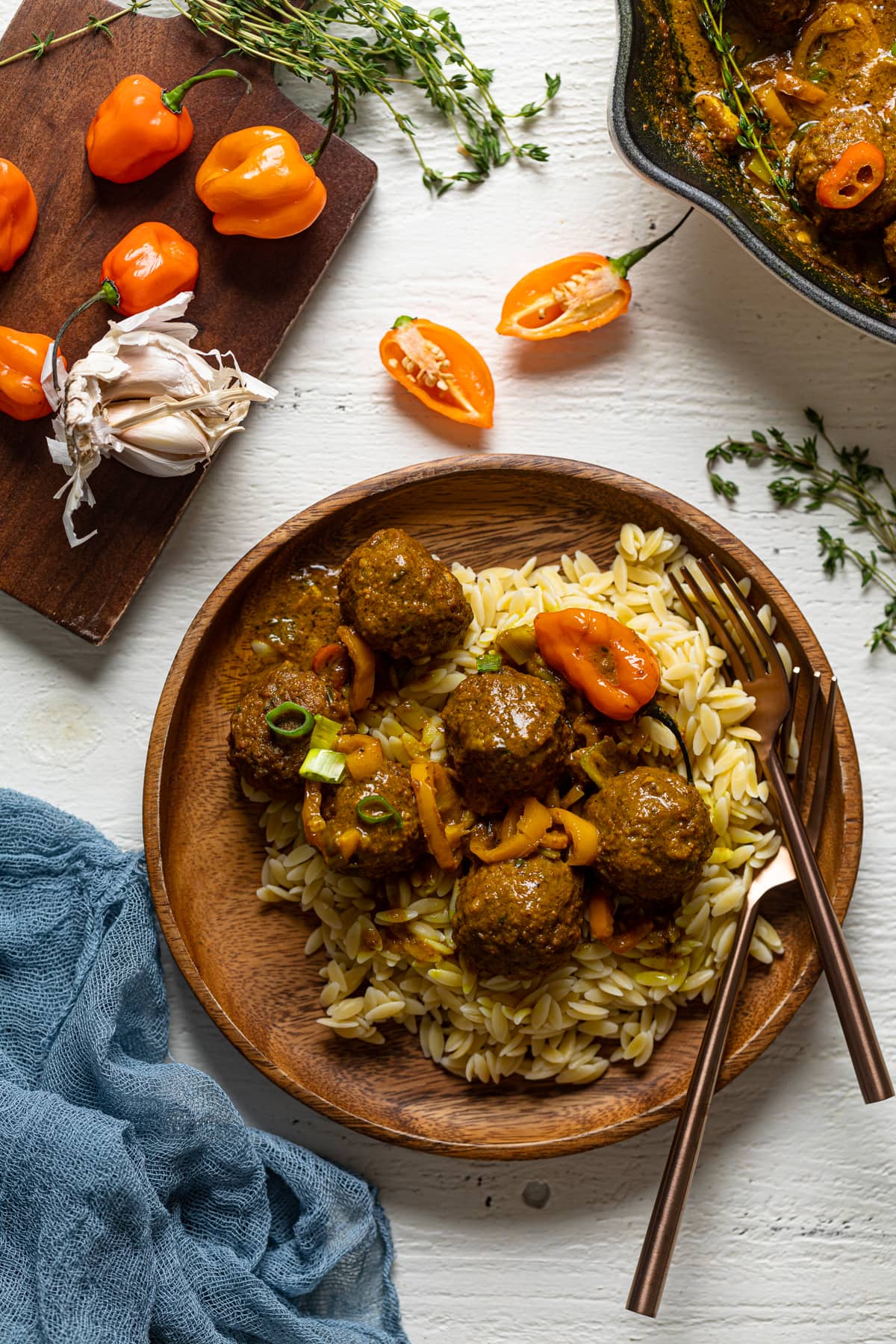 Wooden plate of Spicy Curry Vegan Meatballs with Orzo near garlic bulbs and scotch bonnet peppers