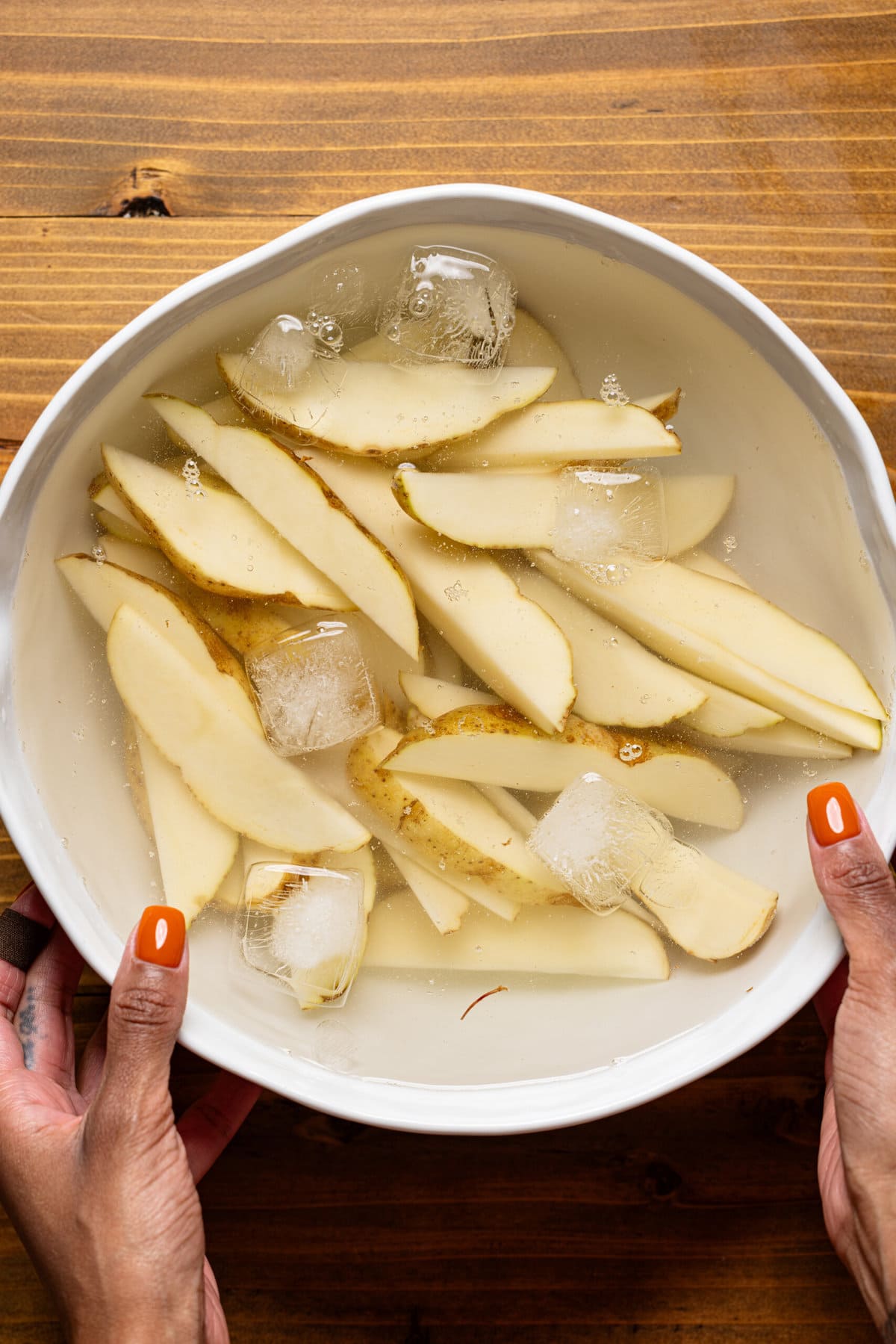 Potato wedges cut and soaked in iced cold water in a white bowl.