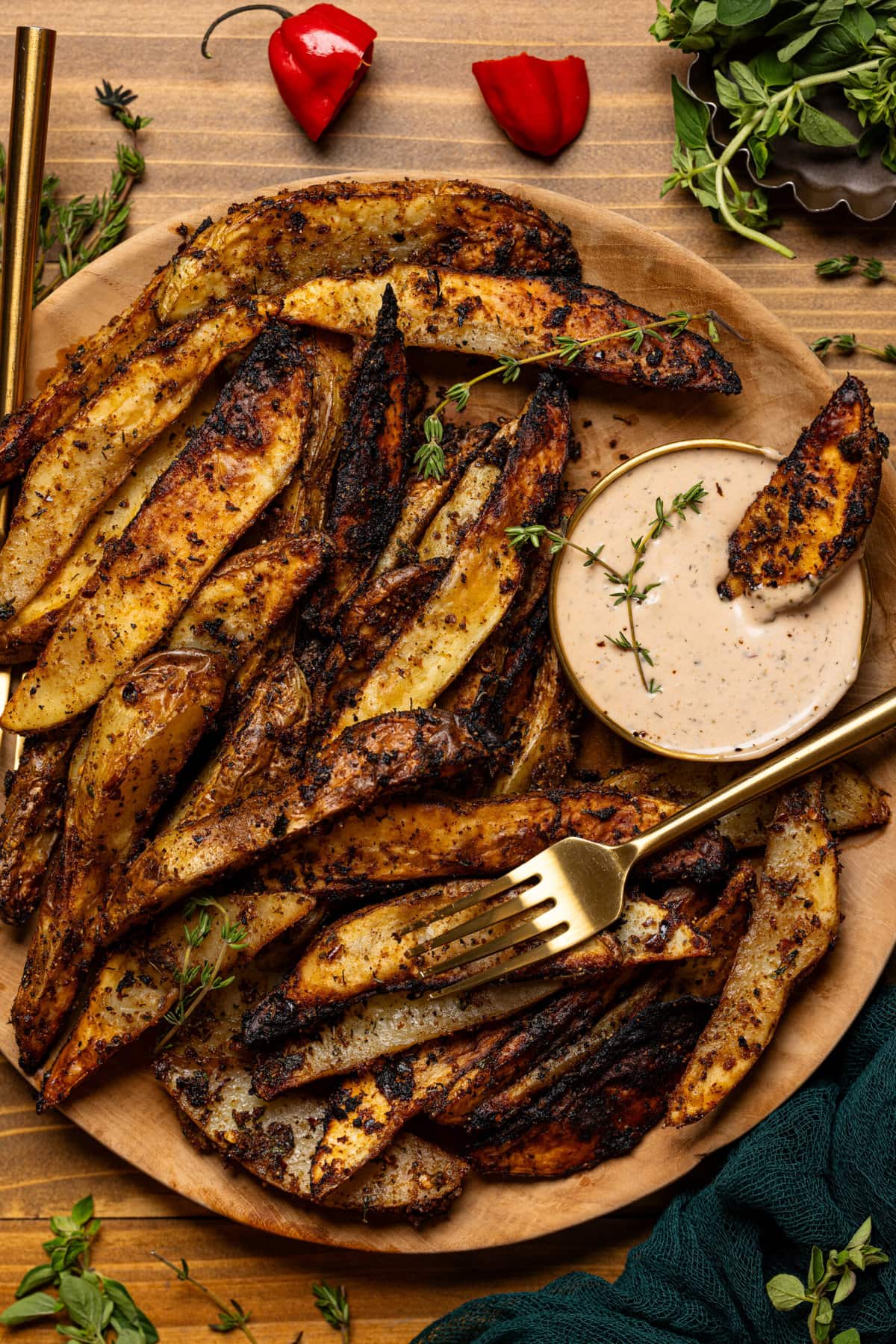 Up close shot of wedges on a brown wooden plate with a two forks and dipping sauce.