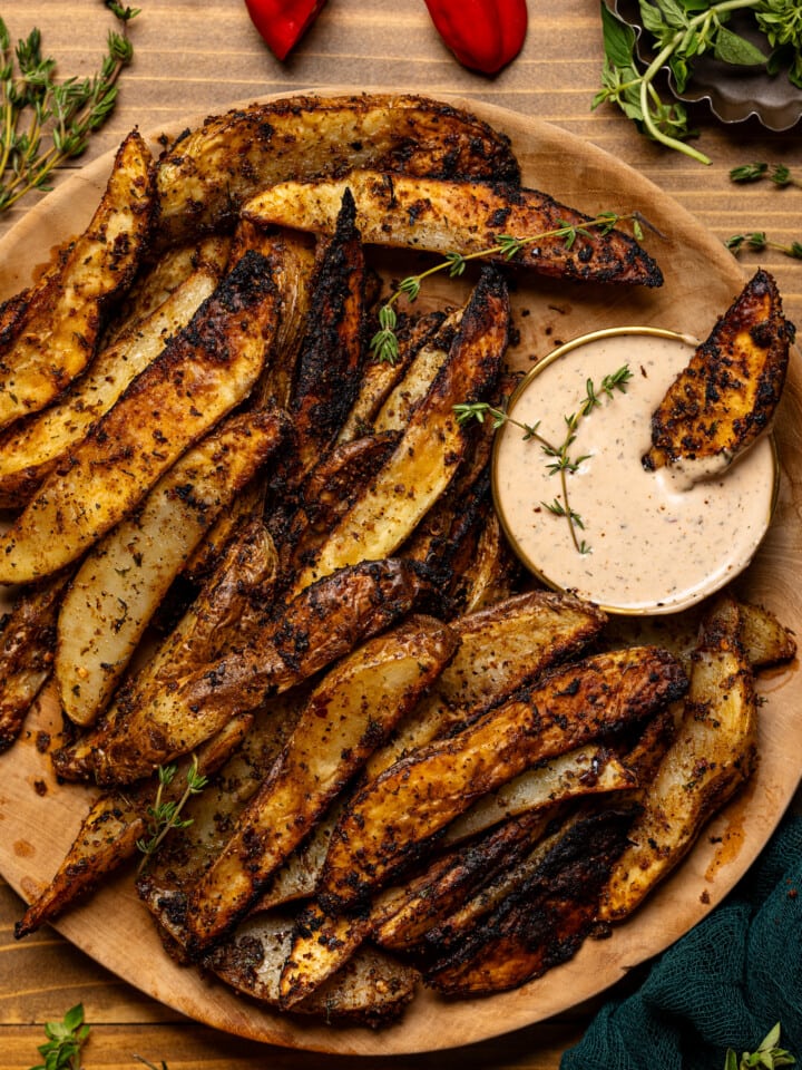 Wedges on a brown wooden plate with dipping sauce and a wedge dipped inside.