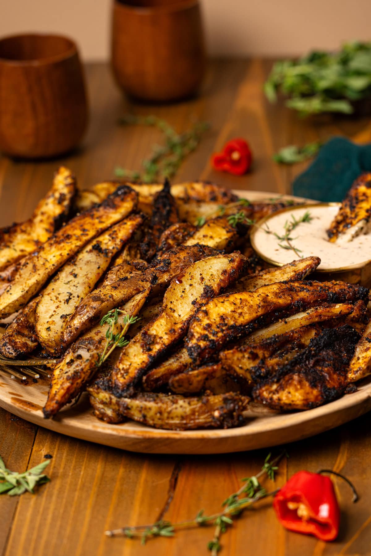 Jerk wedges in a wooden brown plate with a dipping sauce on a brown wooden table.