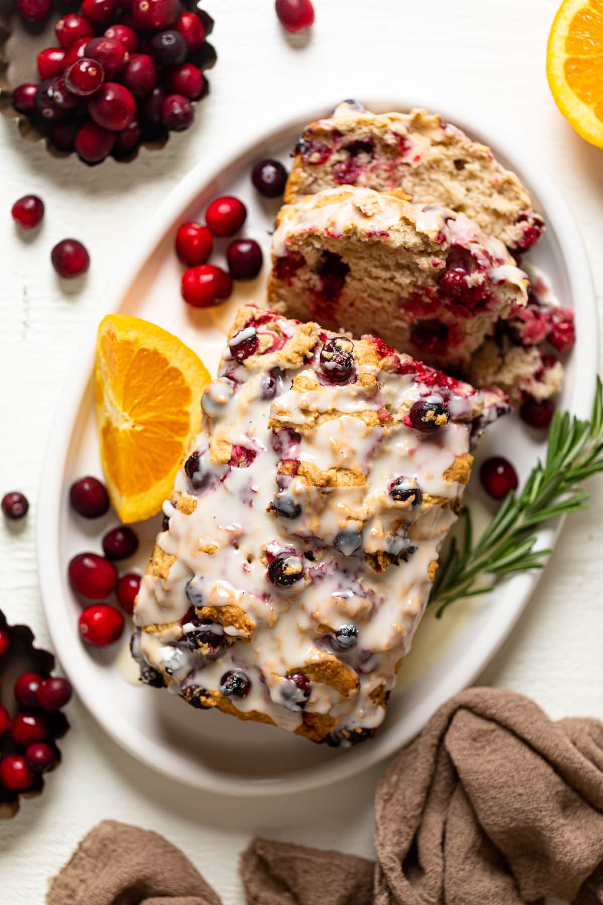 Partially-sliced loaf of Vegan Orange Cranberry Bread drizzled with orange glaze and on a plate