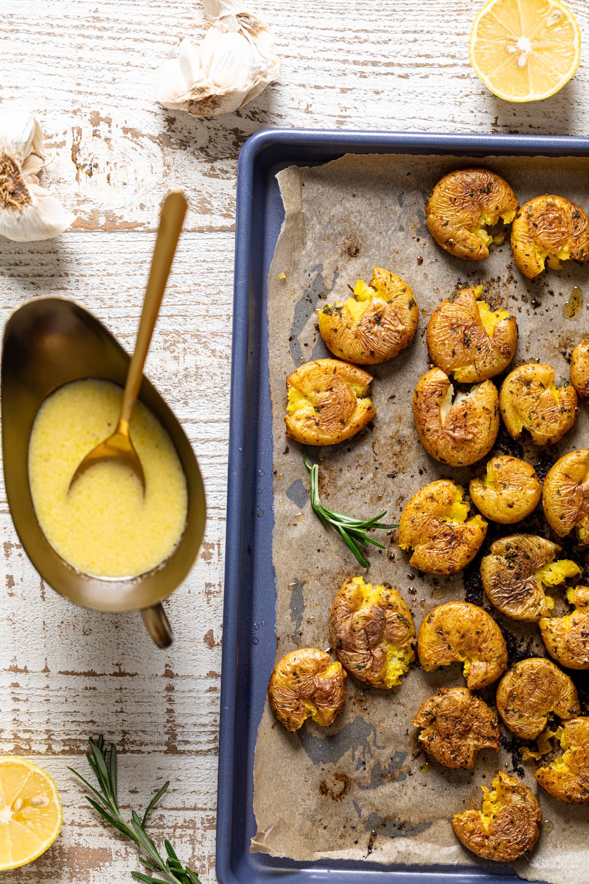 Overhead shot of Garlic Herb Smashed Potatoes on a baking sheet next to a gravy boat of apple cider vinegar dressing