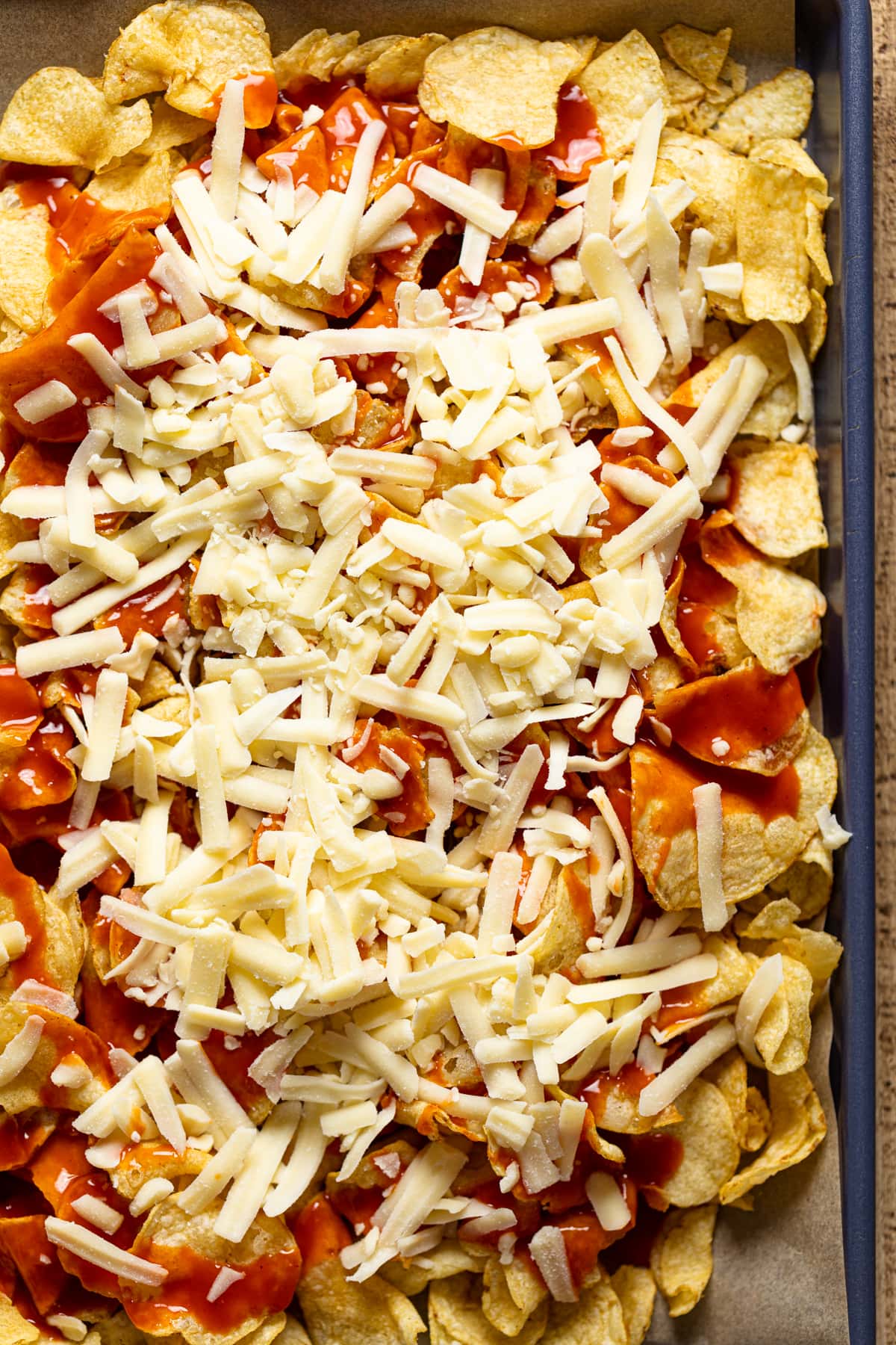 Kettle chips topped with red sauces and cheese on a baking sheet