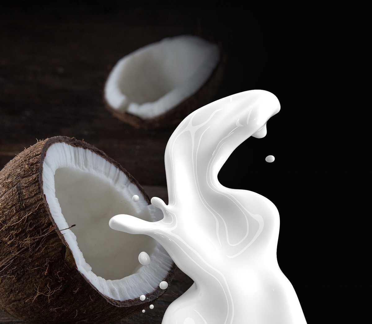 Splash of coconut milk in front of halved coconuts