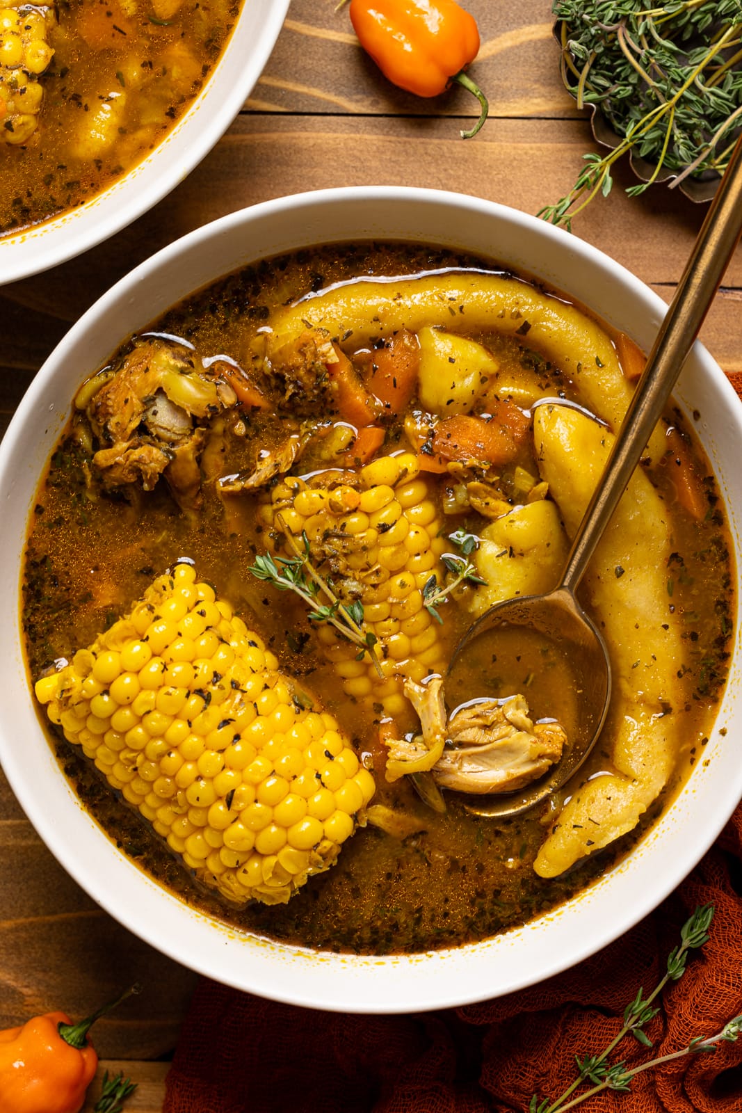 Spoon in a bowl of Jamaican chicken soup on a brown wood table. 