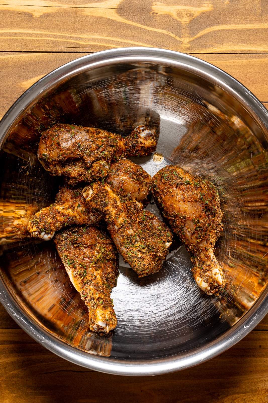 Seasoned chicken in a silver bowl on a brown wood table.