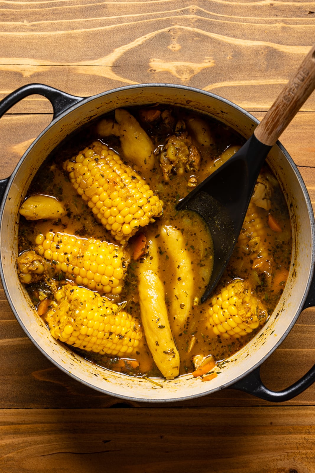 Jamaican chicken Soup in a large Dutch oven with a spoon on a brown wood table.