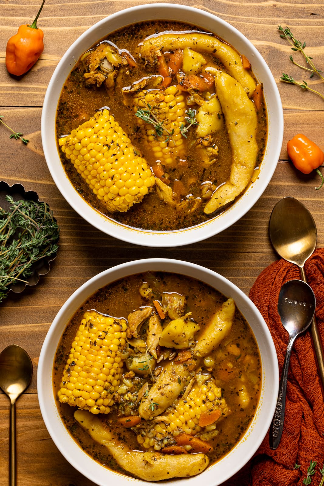 Two bowls of soup on a brown wood table with gold spoons and red napkin.