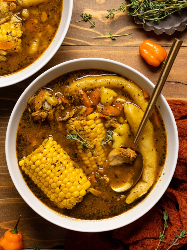 Bowl of Jamaican chicken soup on brown wood table with a spoon and red napkin.