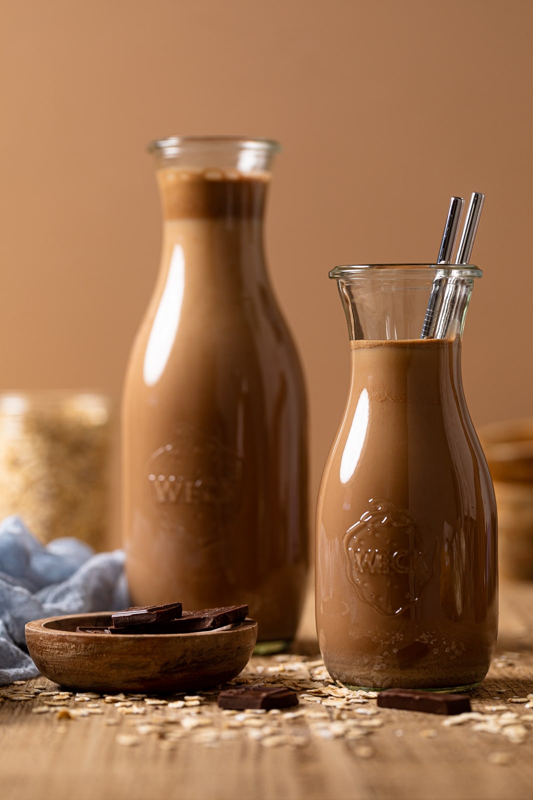 Two glass carafes of Chocolate Oat Milk, one of which has two metal straws