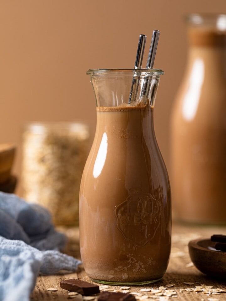 Glass carafe of chocolate oat milk with two metal straws