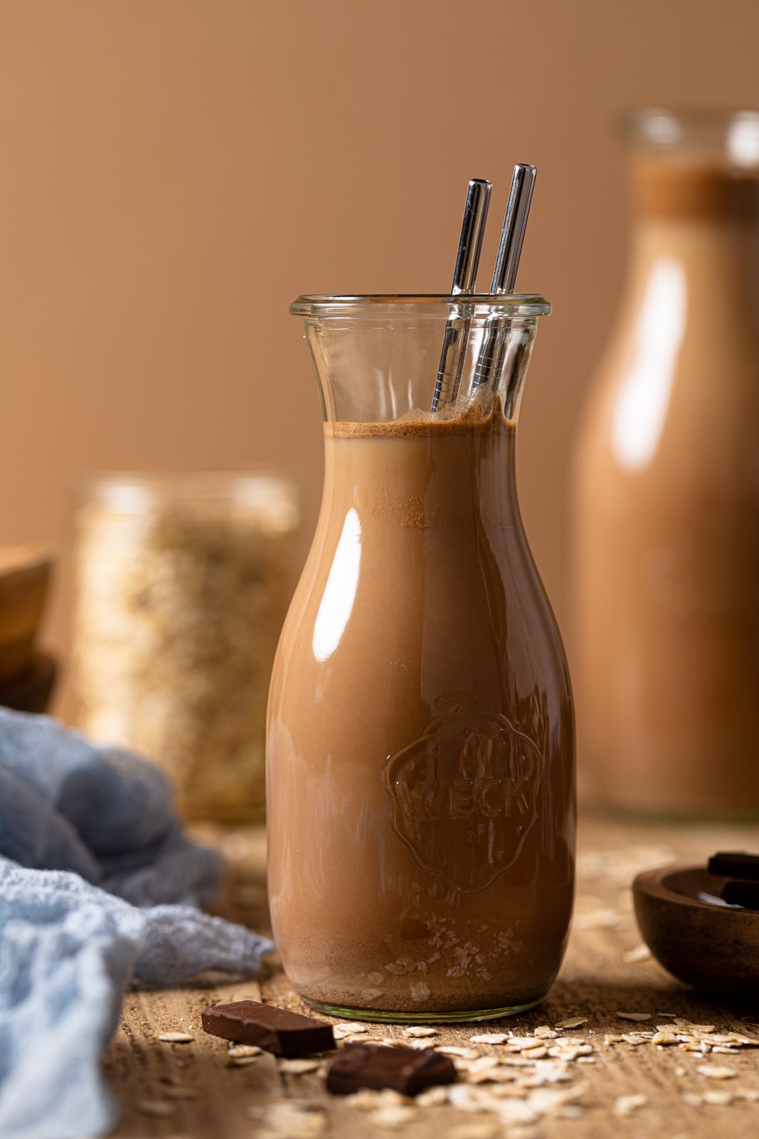Glass carafe of chocolate oat milk with two metal straws