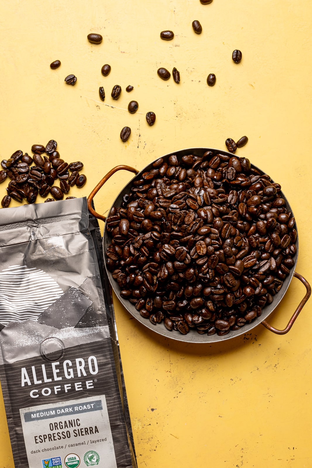 Espresso coffee beans in a bowl and open package on a yellow table.