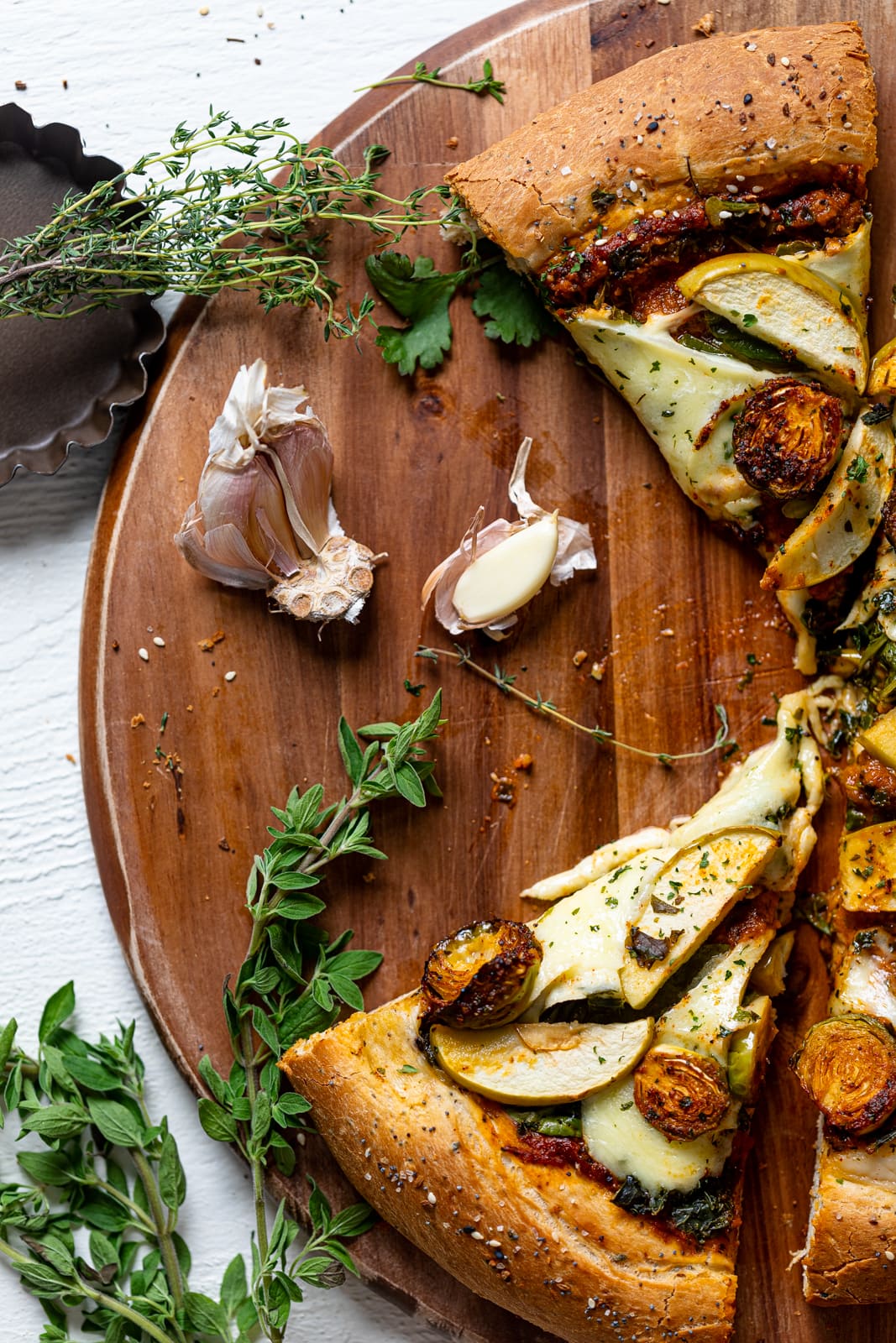 Sliced All Green Pesto Veggie Pizza and garlic cloves on a wooden board