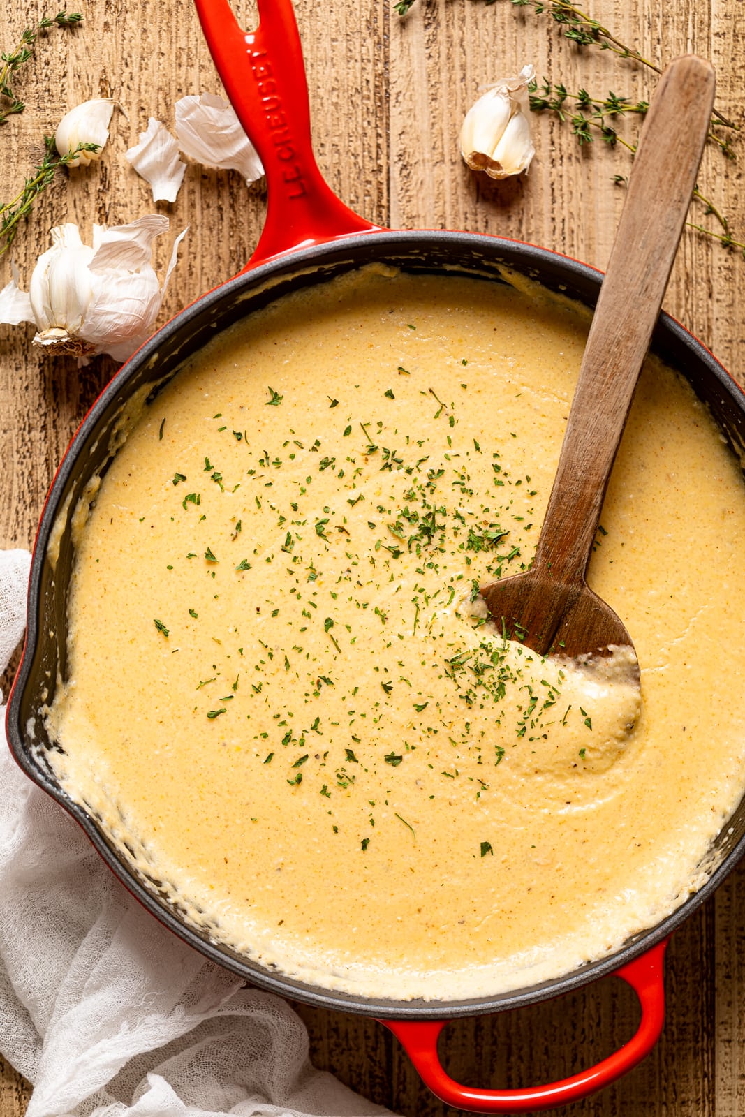 Overhead shot of a wooden spoon stirring Creamy Southern Cheese Grits in a red Le Creuset pan