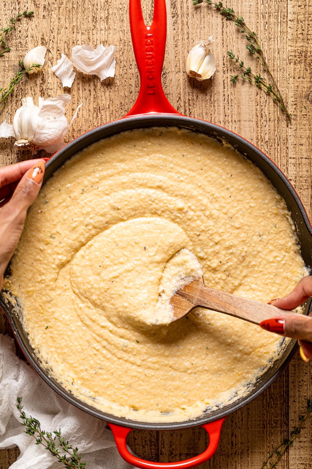 Hands using a wooden spoon to stir in a red Le Creuset pan