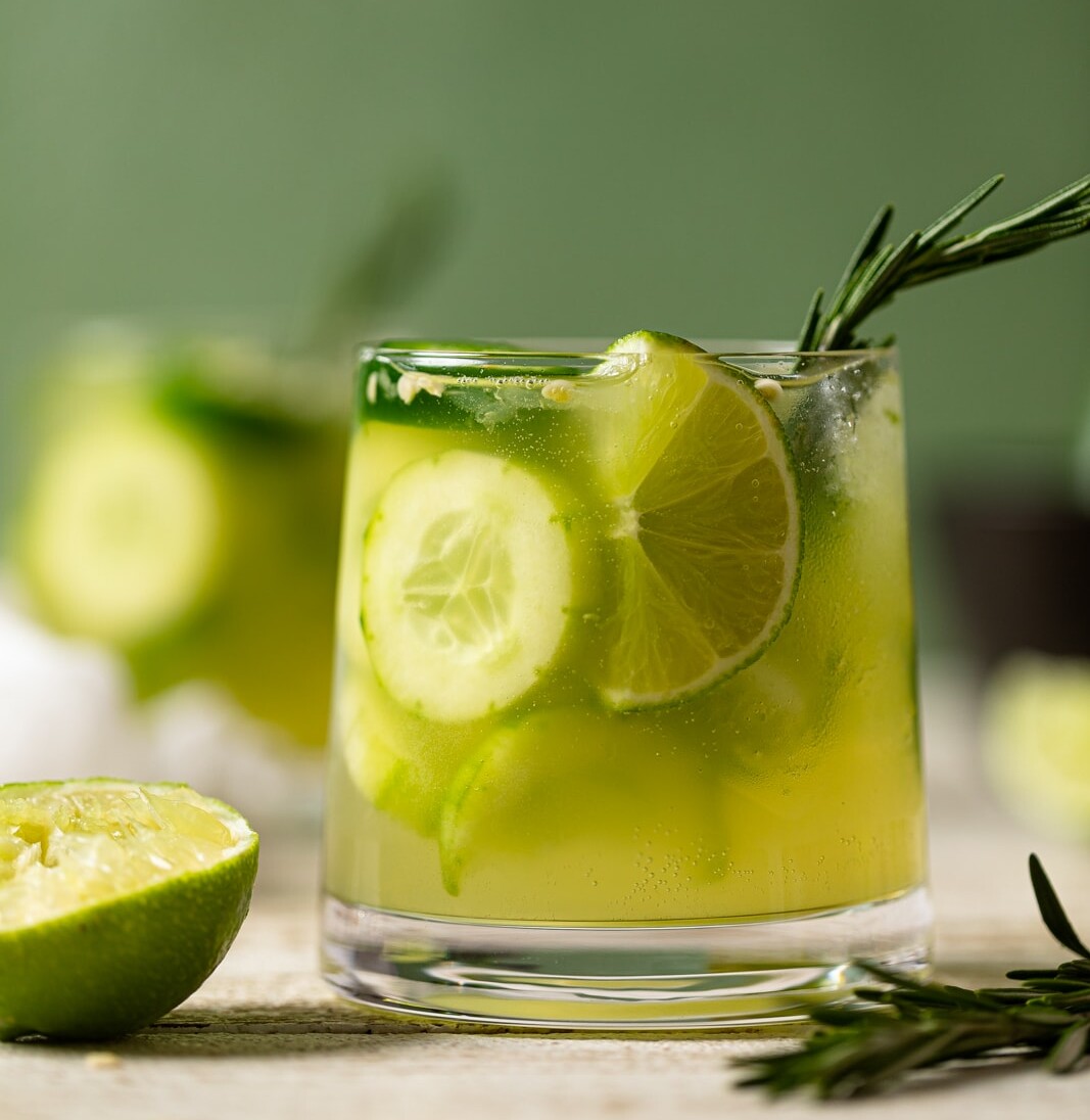 Bright green Spicy Cucumber Mocktail in a small glass stuffed with cucumbers and lime wedges