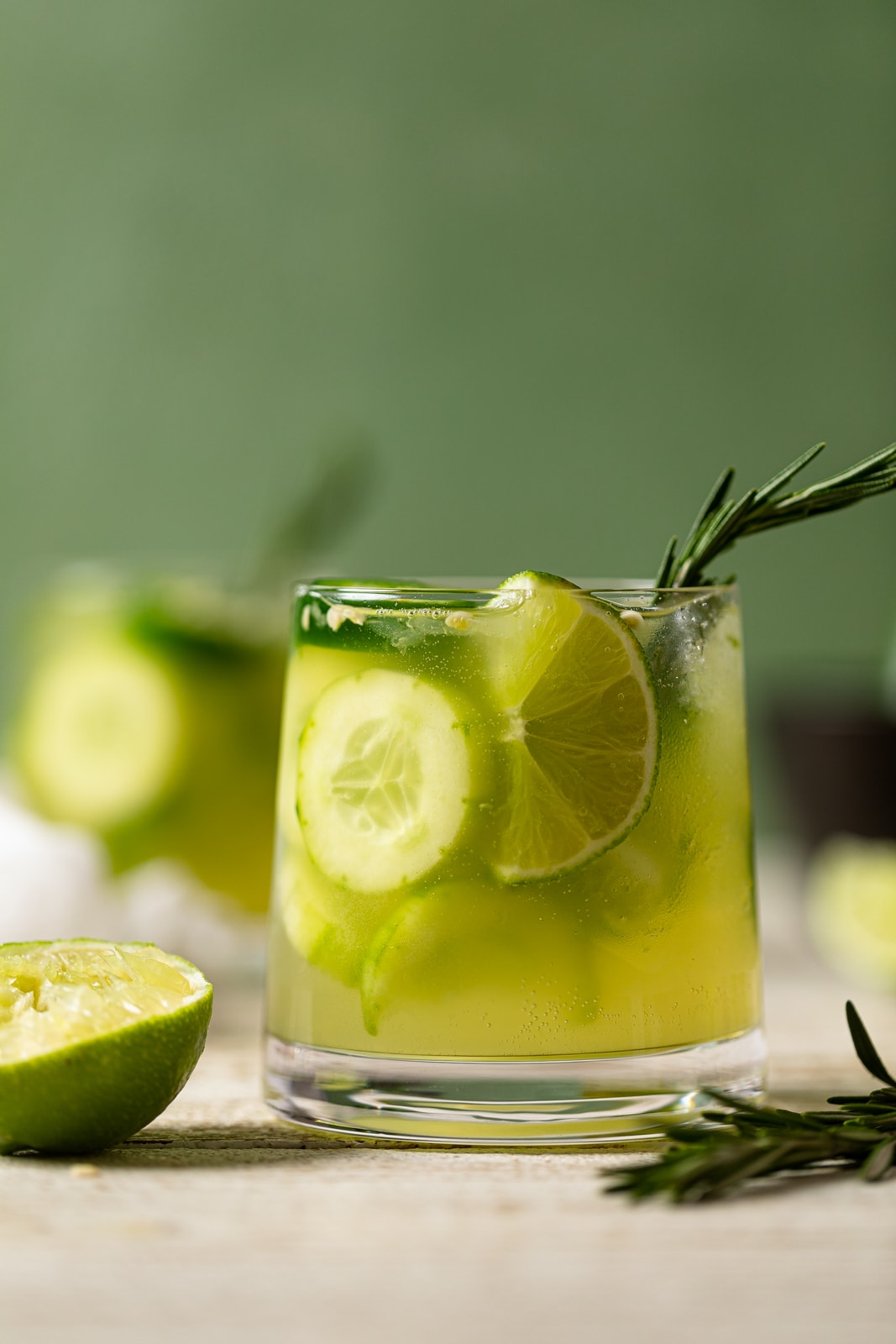 Bright green Spicy Jalapeno Cucumber non-alcoholic cocktail in a small glass stuffed with cucumbers and lime wedges for a summer mocktail