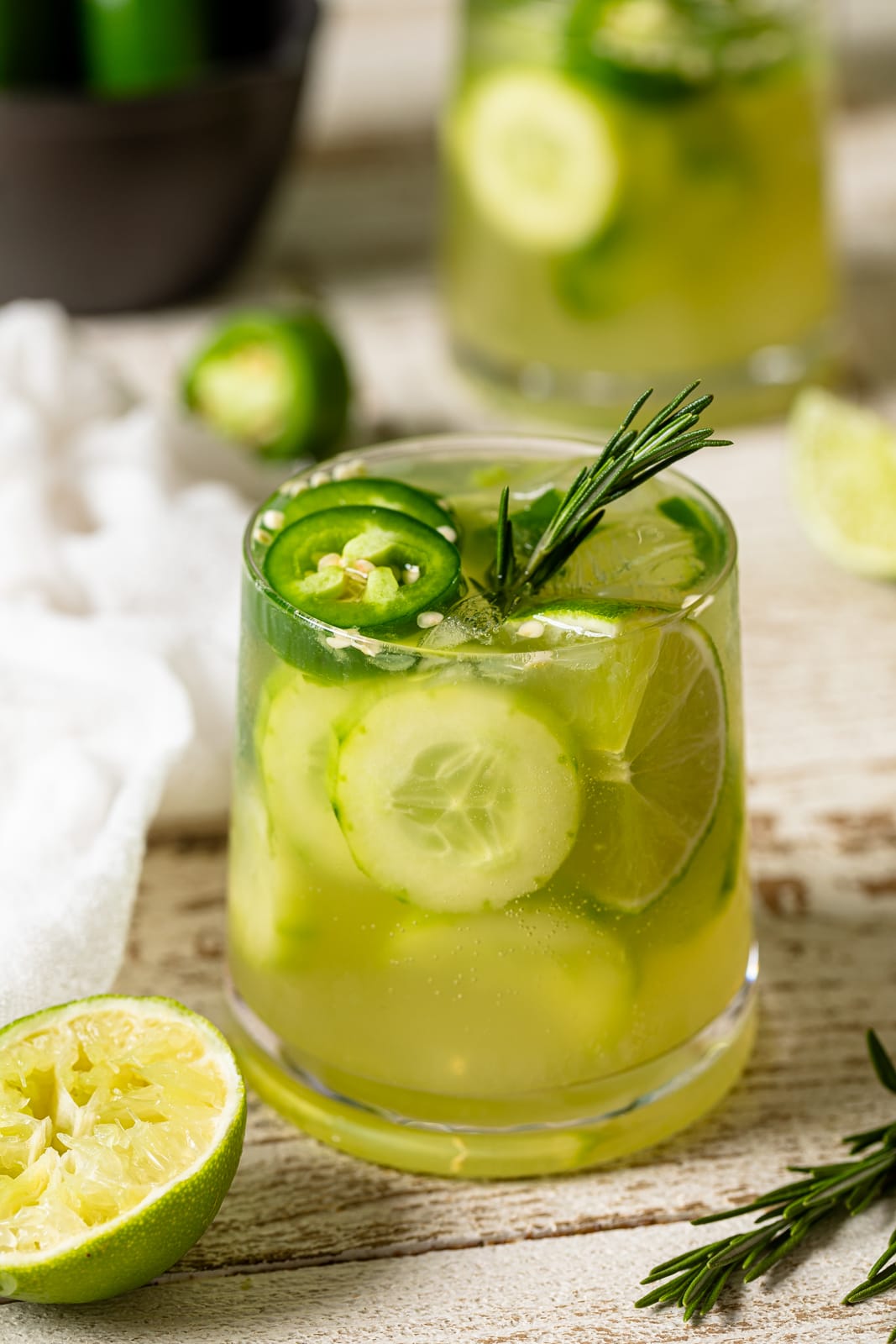 Bright green Spicy Jalapeno Cucumber Mocktail in a small glass stuffed with cucumbers, jalapeno slices, and lime wedges.