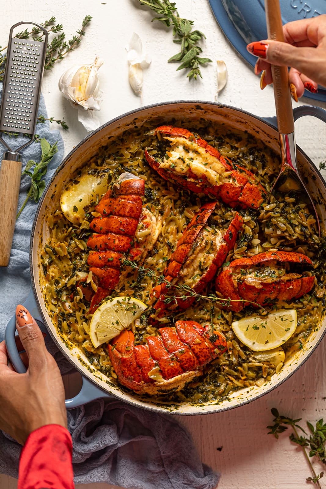 Hand using a spoon to scoop Creamy Lobster and Orzo from a Le Creuset Dutch oven