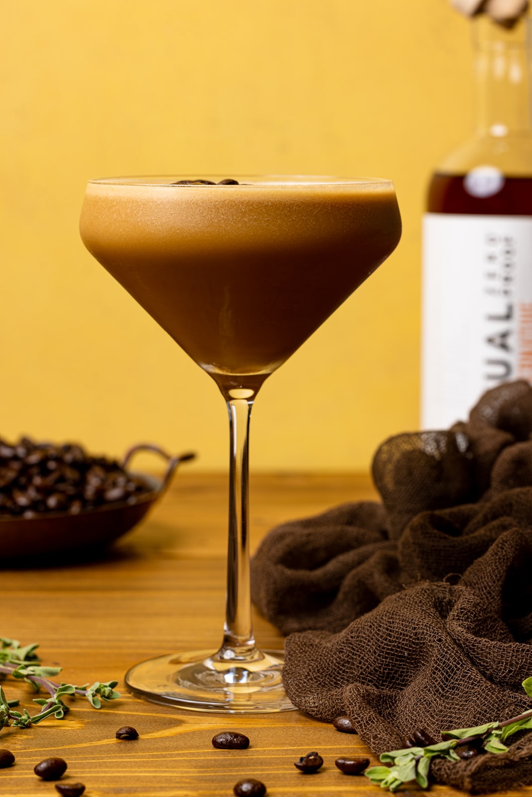 Espresso martini in a glass on a brown wood table with a brown napkin, coffee beans, and Rum alternative.