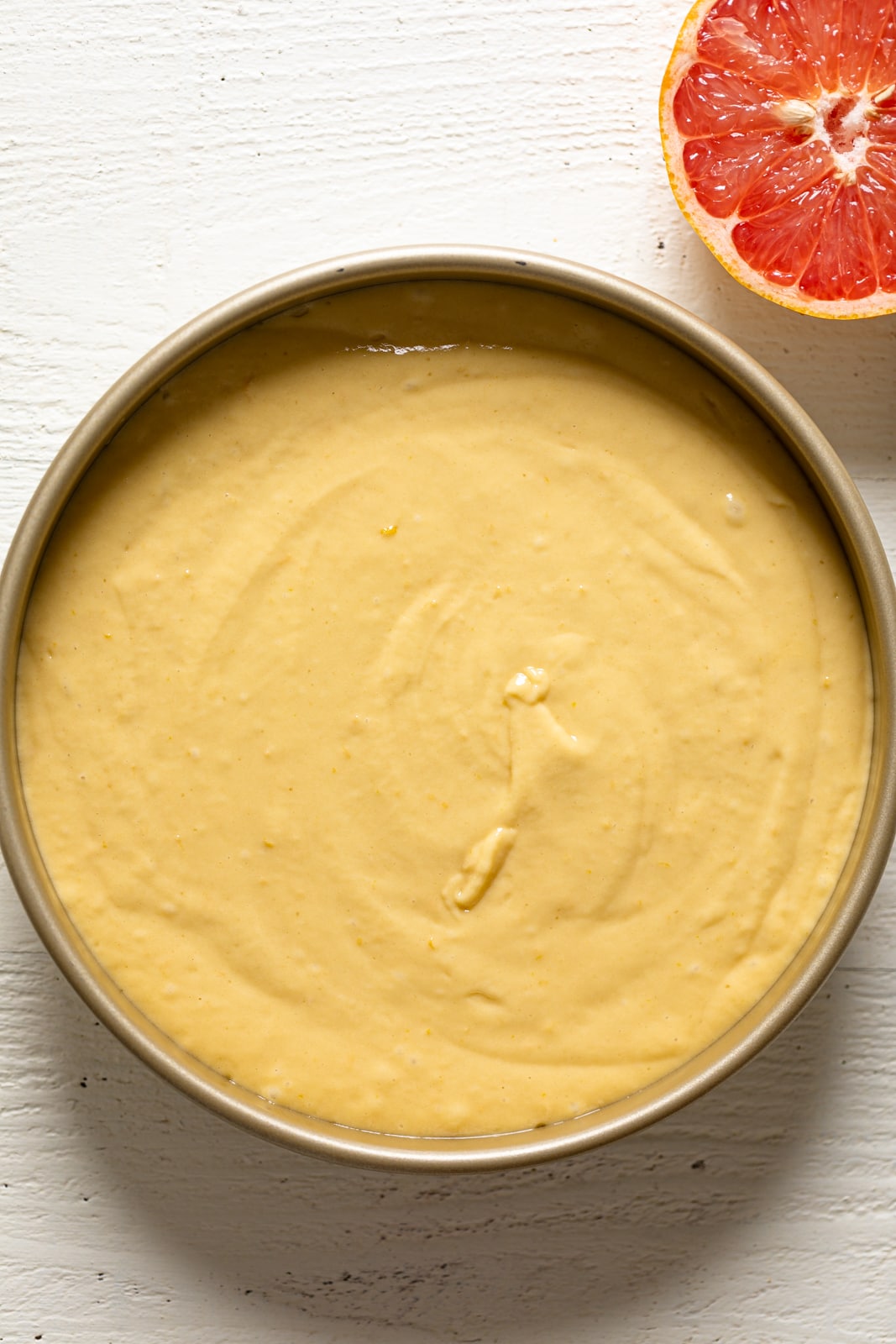 Round pan with Grapefruit Olive Oil Cake batter next to half a grapefruit