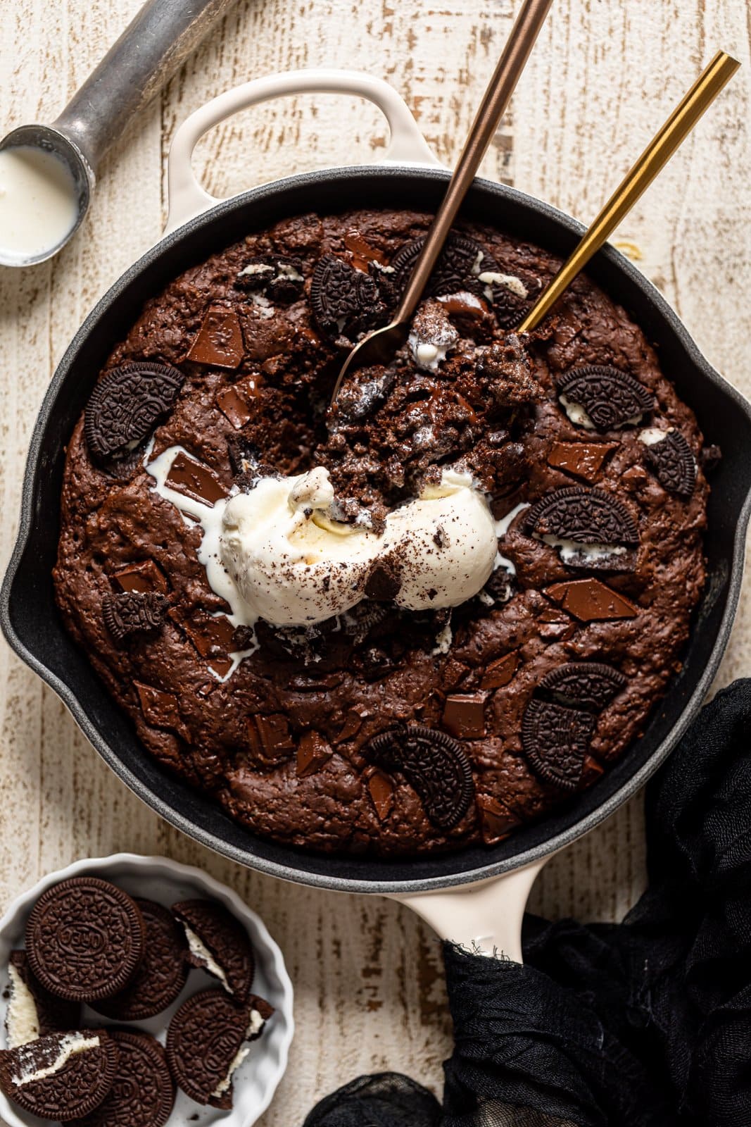 Overhead shot of two spoons dipping into a Chocolate Oreo Skillet Brownie topped with ice cream