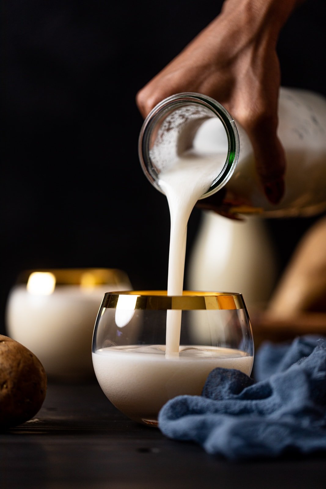 Glass carafe pouring potato milk into a gold-rimmed glass