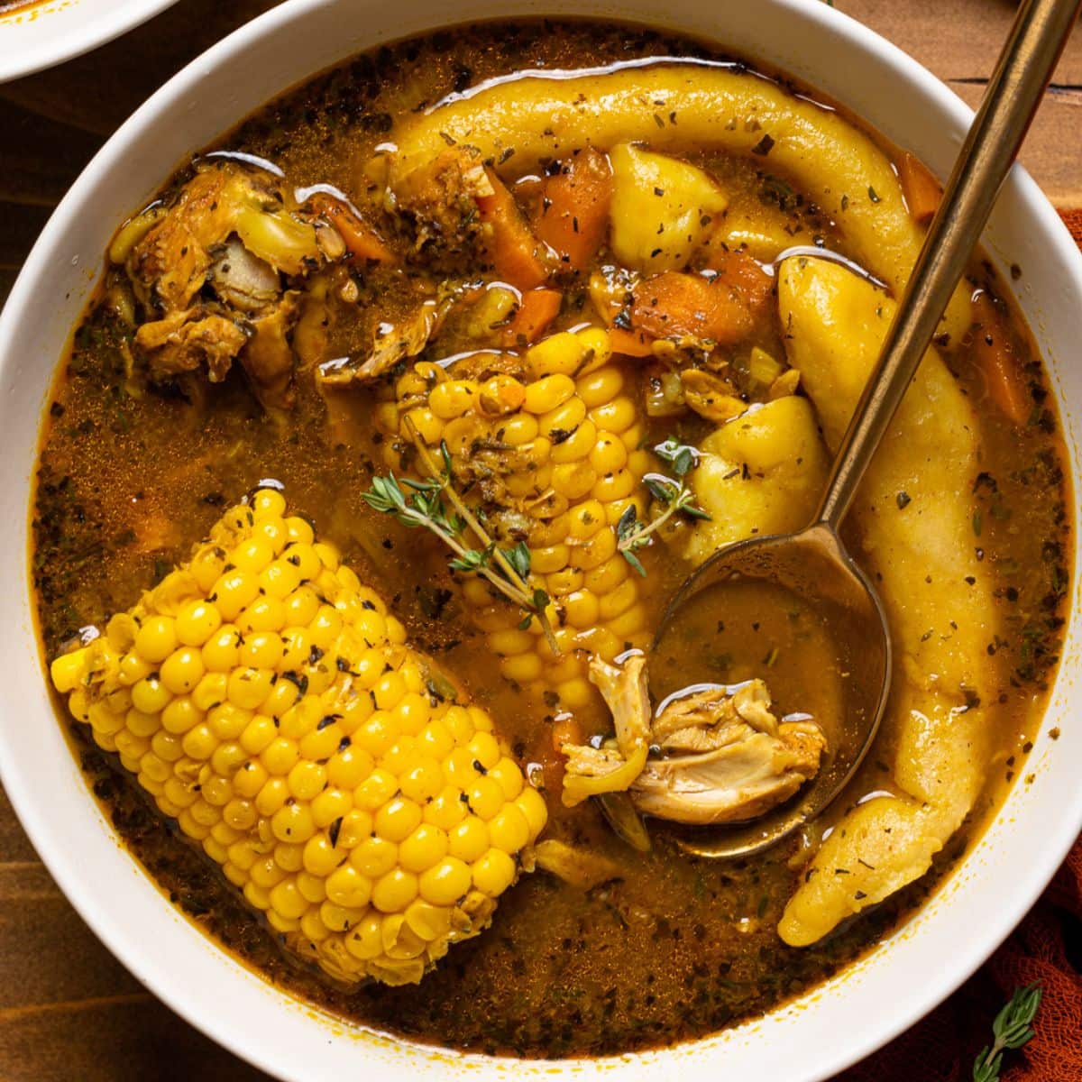 Jamaican chicken soup in a white bowl on a brown wood table.