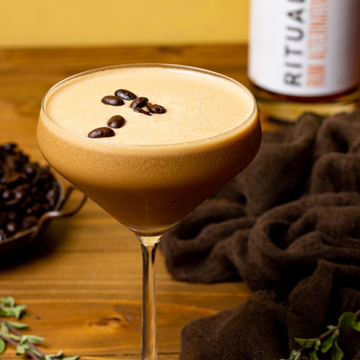 Espresso martini in a glass on a brown wood table with a brown napkin, coffee beans, and Rum alternative.