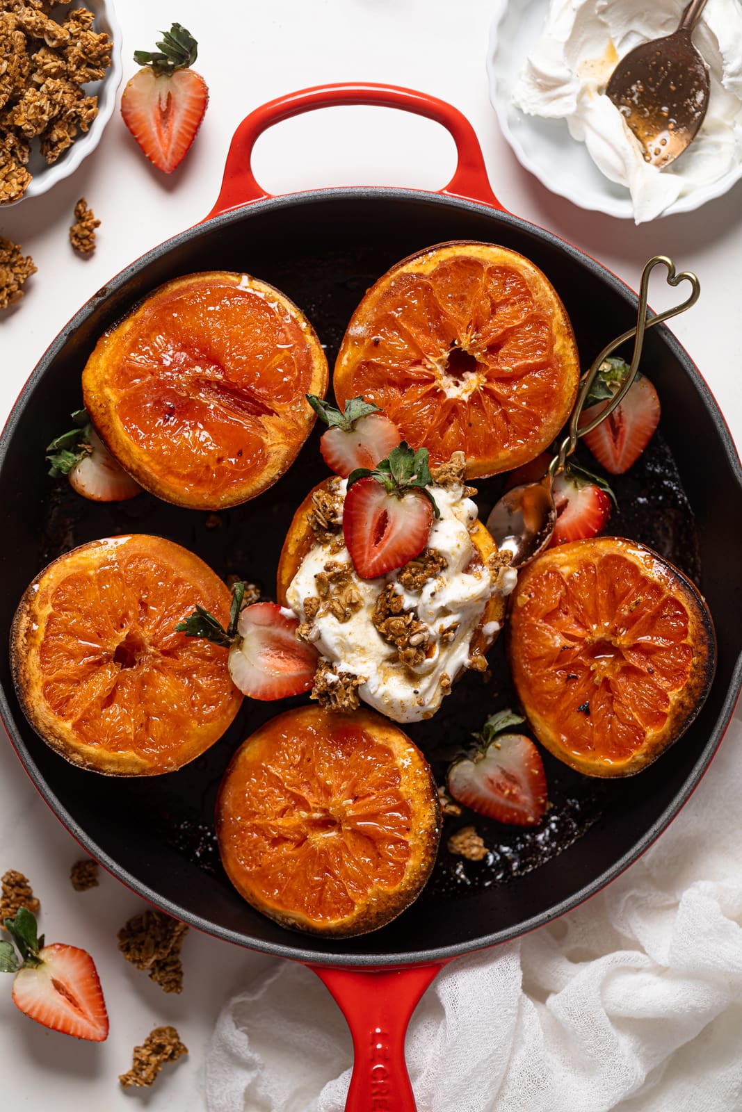 Overhead shot of Broiled Maple Cinnamon Grapefruits with Strawberries, one of which is topped with coconut whipped cream and granola