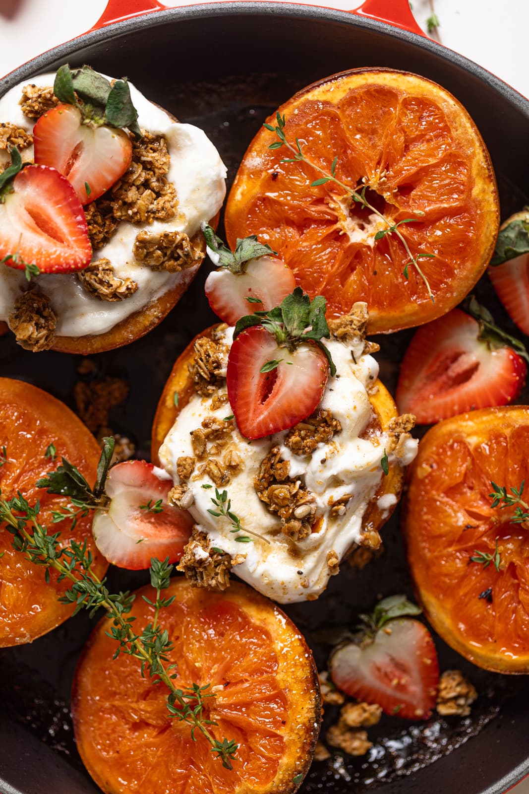 Closeup of Broiled Maple Cinnamon Grapefruits with Strawberries, two of which are topped with coconut whipped cream and granola