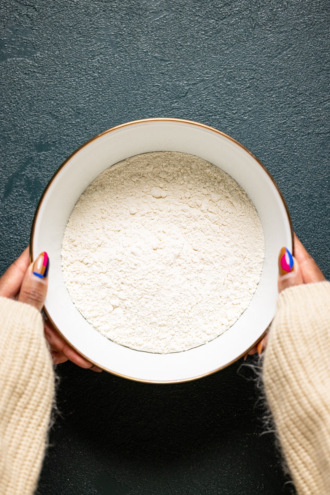 A white bowl with flour being held on a dark green table.
